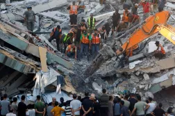 İnsanlar, bugün Gazze kentinde çöken binanın enkazı altında mahsur kalanları kurtarmaya çalışan sivil savunma ekiplerinin çevresinde toplanıyor (Reuters)