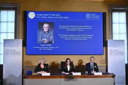 Eva Olsson, Ellen Moons, and Mark Pearce sit in front of a screen displaying Francis Halzen as the recipient of the 2026 Nobel Prize in Physics during a press conference at the Royal Swedish Academy of Sciences in Stockholm, Sweden, on October 6, 2026. (Photo by Christine OLSSON / TT NEWS AGENCY / AFP) 