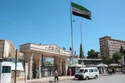 14 Mayıs 2025’te Halep Üniversitesi girişinin yakınından geçen bir kadın ve Suriye bayrağı (Reuters)