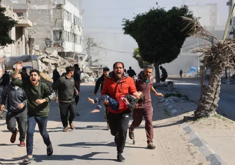 فلسطيني يحمل طفلة جريحة بعيدا عن موقع وسط قطاع غزة لجأ إليه نازحون واستهدفته ضربة إسرائيلية أمس (أ.ف.ب)