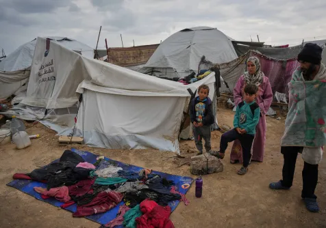 رأفت علوان (32 عاماً) على اليمين وعائلته يقفون خارج خيمتهم بينما ملابسهم ملقاة على غطاء بلاستيكي لتجف في مخيم مؤقت للنازحين الفلسطينيين أقيم على الشاطئ خلال صباح بارد في مدينة غزة (أ.ب)