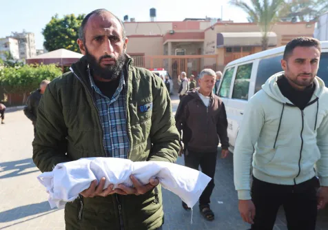 فلسطيني يحمل جثمان رضيع توفي بسبب البرد القارس في خان يونس جنوب غزة (رويترز)