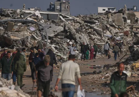 فلسطينيون يسيرون وسط الدمار الذي خلَّفته الغارات الإسرائيلية على قطاع غزة (أ.ب)