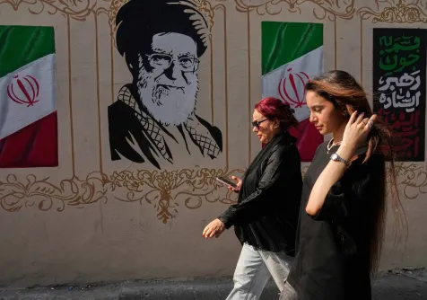 إيرانيتان تمران قرب صورة للمرشد الإيراني السابق علي خامنئي الذي قُتل في الضربات الأميركية - الإسرائيلية في 28 فبراير وأعلام إيرانية وسط طهران - 20 أغسطس 2026 (أ.ب)