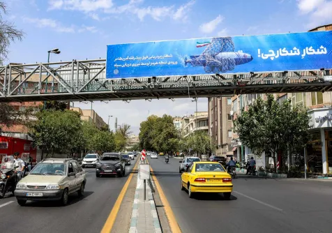 سيارات تتحرك على طول شارع بالقرب من جسر للمشاة يحمل لوحة إعلانية مناهضة لأميركا في طهران (أ.ف.ب)