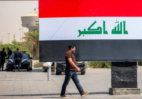 عراقي يمر أمام لوحة إعلانية تحمل العلم العراقي في ساحة التحرير بوسط بغداد 22 سبتمبر 2026 (أ.ف.ب)