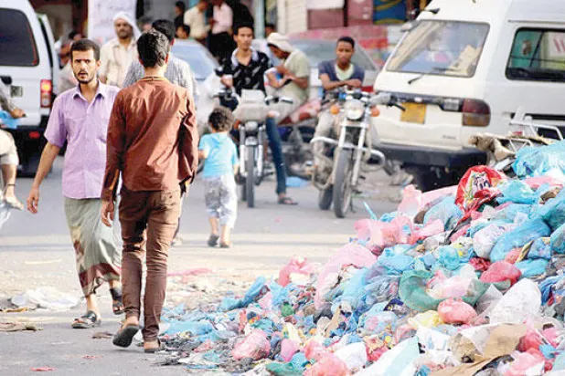 يمنيون يمرون بمحاذاة أكوام من النفايات في شارع رئيسي أمس في تعز ثالث أكبر مدينة يمنية (أ ف ب)