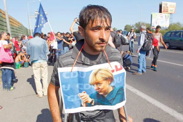 مهاجر يحمل صورة المستشارة الألمانية ميركل خلال عبوره شوارع بودابست بهنغاريا أمس (إ.ب.أ)