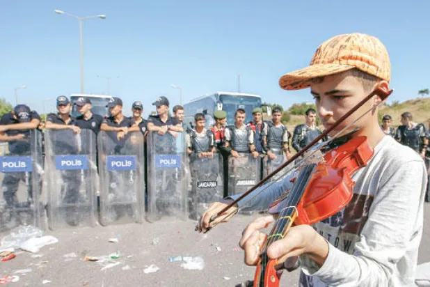 طفل سوري يعزف الكمان، فيما يسعى مئات اللاجئين إلى السير نحو الحدود التركية الغربية أمس (أ.ب)