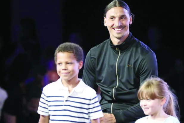 إبراهيموفيتش  مع طفلين يعرضان ماركة ملابسه الرياضية الجديدة (أ.ف.ب)