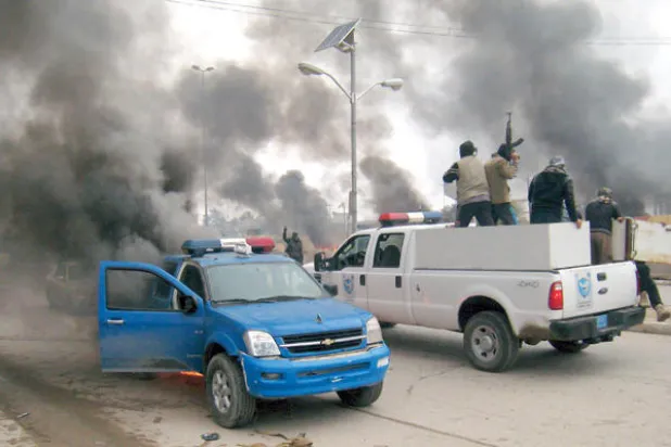 عناصر من {داعش} يعتلون سيارة للشرطة أمام مبنى البلدية الذي تلفه سحب الدخان في الفلوجة في صورة تعود لعام 2014 (أ.ب)