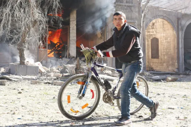 شاب من حي باب النيرب في القسم المحاصر من حلب يمر بمنزل يحترق في أعقاب قصف طيران النظام للمنطقة أول من أمس (إ.ف.ب)