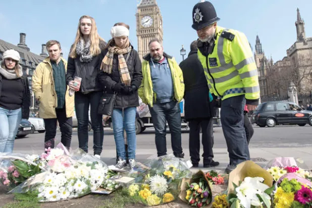 ضابط شرطة من {اسكوتلنديارد} ومارة ينظرون إلى أكاليل الورود في موقع الهجوم على البرلمان البريطاني أمس