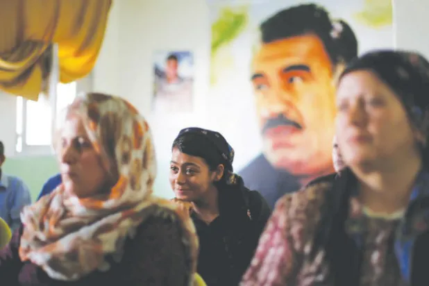 نساء من حي الشيخ مقصود في حلب يستمعن إلى محاضرة وفي الخلفية صورة الزعيم الروحي لحزب «الاتحاد الديمقراطي» الكردي (رويترز)