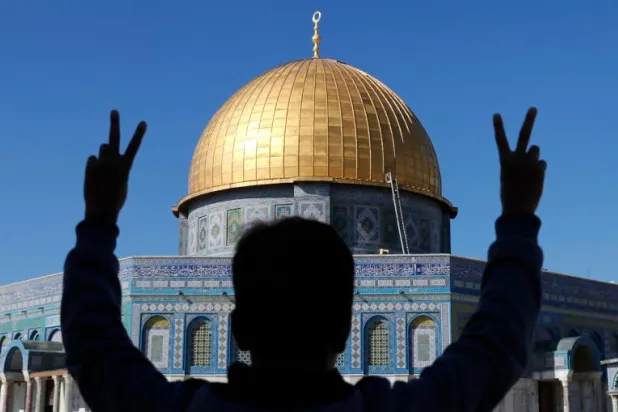 شاب فلسطيني يلوح بعلامة «النصر» أمام المسجد الأقصى في البلدة القديمة بالقدس (أ.ف.ب)