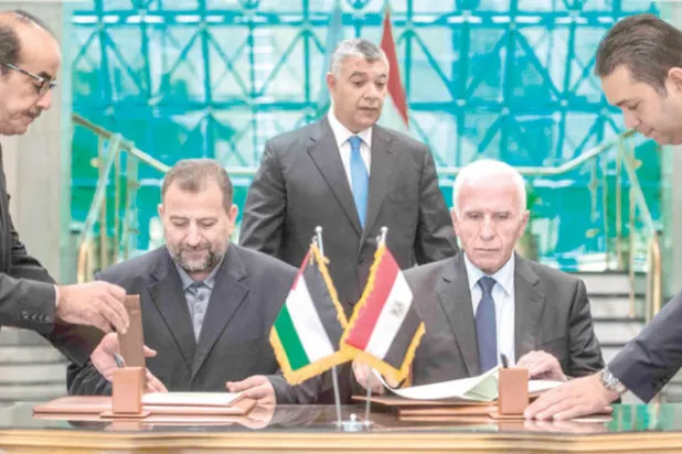 رئيس الاستخبارات العامة المصرية الوزير خالد فوزي يتوسط رئيسي وفدي «فتح» و «حماس» خلال توقيعهما اتفاق المصالحة في القاهرة (أ.ف.ب)