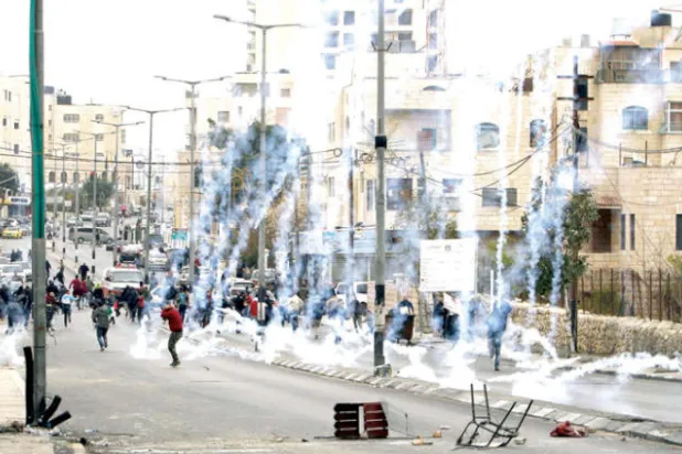 محتجون يحاولون الاحتماء من قنابل الغاز خلال مواجهات مع قوات الاحتلال في الضفة الغربية أمس (أ.ف.ب)