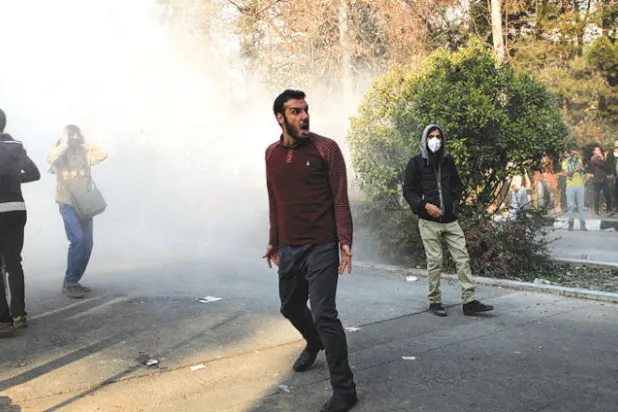 طلاب في مواجهة الغاز المسيل للدموع أمام بوابة جامعة طهران وسط شارع انقلاب في 30 ديسمبر الماضي (أ.ب)