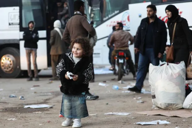 طفلة سورية تقف أمام الحافلات عند وصولها إلى قلعة المضيق غرب مدينة حماة (أ.ف.ب)