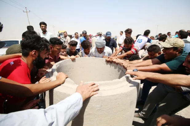 محتجون عراقيون يحاولون تحريك كتل إسمنتية لإغلاق الطريق خلال مظاهرة في جنوب البصرة (رويترز)