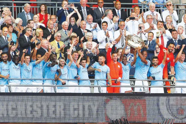 لاعبو مانشستر سيتي على منصة التتويج في ويمبلي يحتفلون بالدرع الخيرية (رويترز)