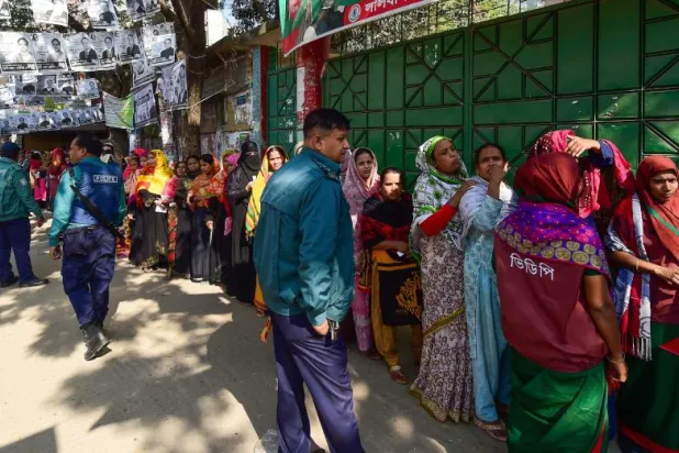 الناخبون البنغلاديشيون يقفون خارج مركز اقتراع بينما يراقب مسؤولو الأمن في داكا (أ.ف.ب)