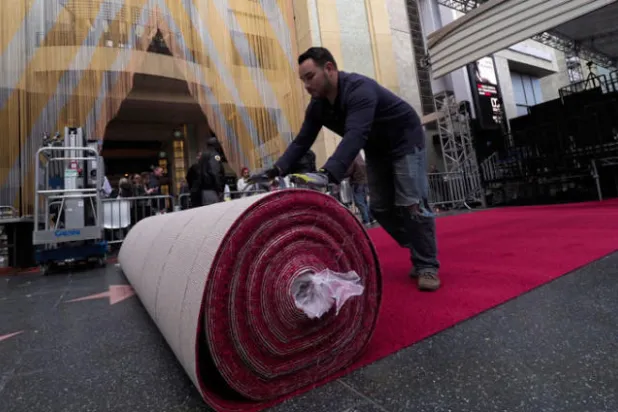 عمال يفرشون السجادة الحمراء المعدّة لممشى المشاهير في حفل الأوسكار (إ.ب.أ)
