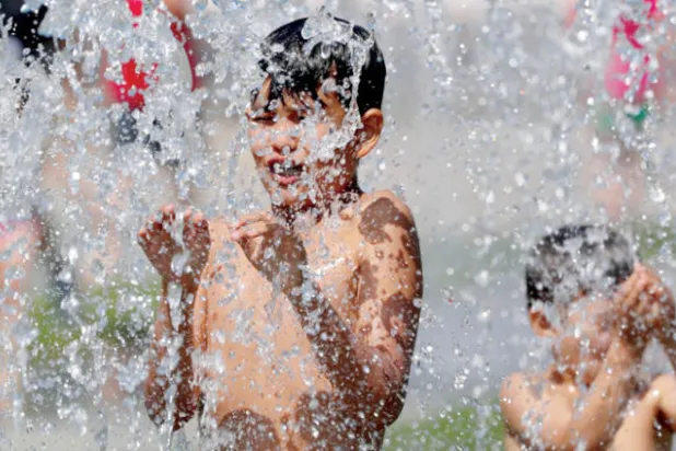 أطفال يتبردون في نافورة خلال يوم صيف حار في برلين (رويترز)