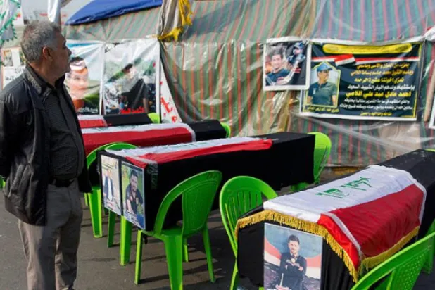 ایک عراقی کو گذشتہ روز بغداد کے تحریر اسکوائر میں مظاہرین میں سے متاثرین شدہ کے علامتی تابوت پر غور کرتے ہوئے دیکھا جا سکتا ہے