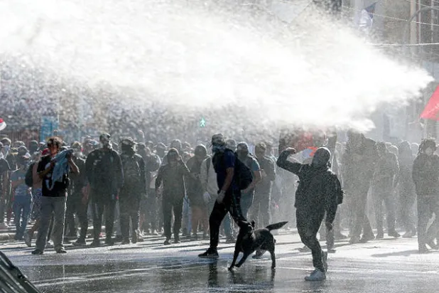 متظاهرون في تشيلي أثناء تعرضهم للمياه بخراطيم قوات الأمن لتفريقهم في أكتوبر الماضي (رويترز)