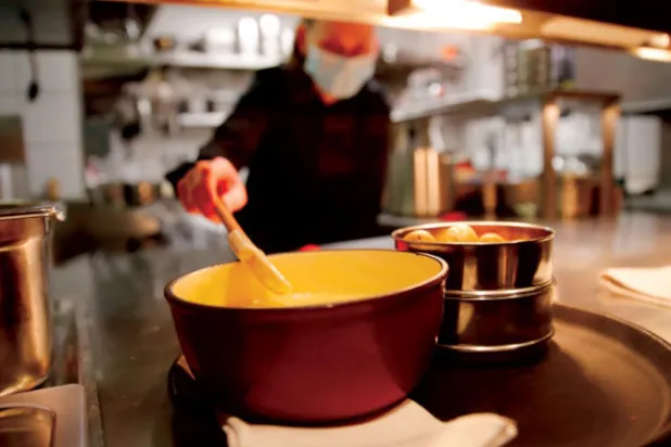 طباخ يرتدي قناعاً واقياً وهو يحضر طبق الفوندو (أ.ف.ب)