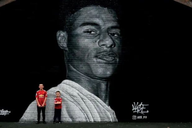 طفلان أمام جدارية لراشفورد في مدينة مانشستر (أ.ف.ب)