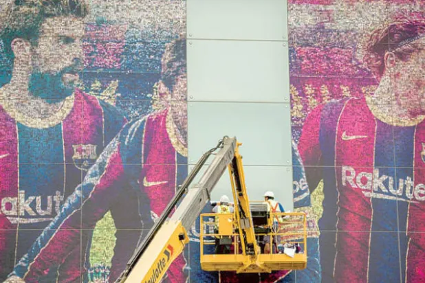 عمال ينزعون صورة ميسي عن واجهة ملعب «كامب نو» (الغارديان)