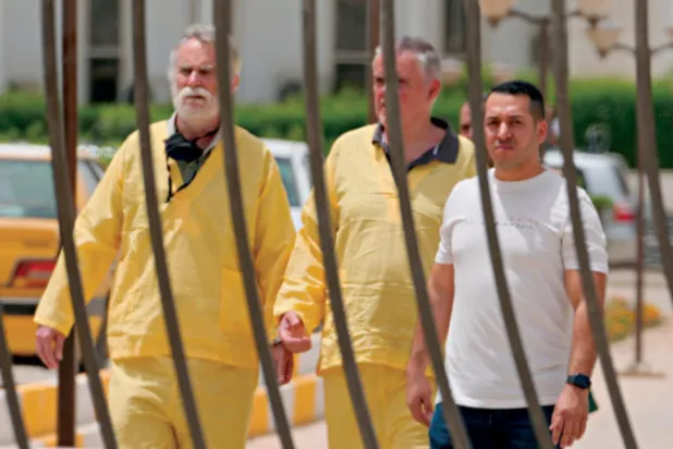 المتهمان البريطاني والألماني في الرداء الأصفر عند خروجهما من قاعة المحكمة في بغداد أمس (أ.ب)