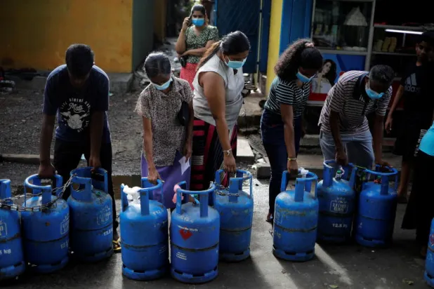 أشخاص يحملون أسطواناتهم الفارغة في طابور لشراء الغاز في كولومبو (رويترز)
