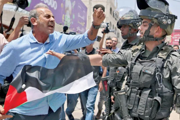 فلسطيني يشتبك مع عنصر من حرس الحدود الإسرائيلي في بلدة حوارة بالضفة الغربية أمس (أ.ف.ب)