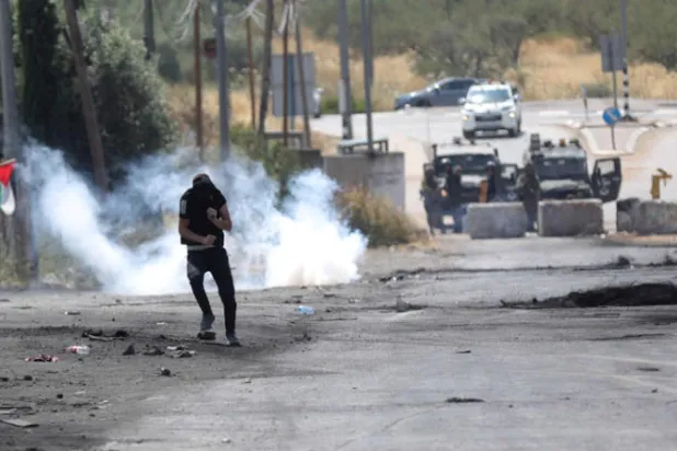 فلسطيني يسعى للاحتماء خلال مواجهات مع القوات الإسرائيلية في قرية بيتا بالضفة (إ.ب.أ)