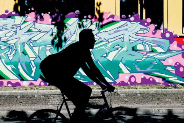 رجل يقود دراجته الهوائية أمام جدارية في أحد شوارع العاصمة الألمانية برلين (إ.ب.أ)