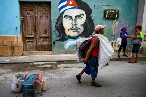 كوبي يجرّ مواد بلاستيكية لإعادة تدويرها أمام لوحة جدارية لغيفارا في أحد شوارع هافانا (أ.ف.ب)