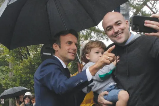 ایک فرانسیسی شہری اپنے بیٹے کو اٹھائے ہوئے ہے اور پولنگ سٹیشن کے باہر صدر ایمانوئل میکرون کے ساتھ "سیلفی" لے رہا ہے۔ (ا ب ا)