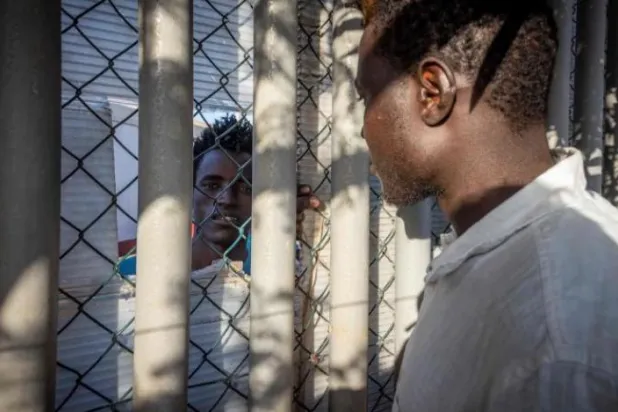 Melilla’daki sığınmacılar için hazırlanan geçici bir merkezde bir göçmen duvarın arkasından konuşuyor (AFP)