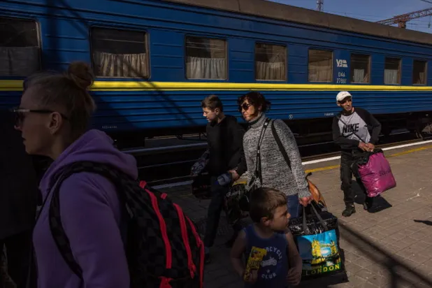 مسافرون يحملون أمتعتهم أمام قطار متجه إلى غرب أوكرانيا (إ.ب.أ)