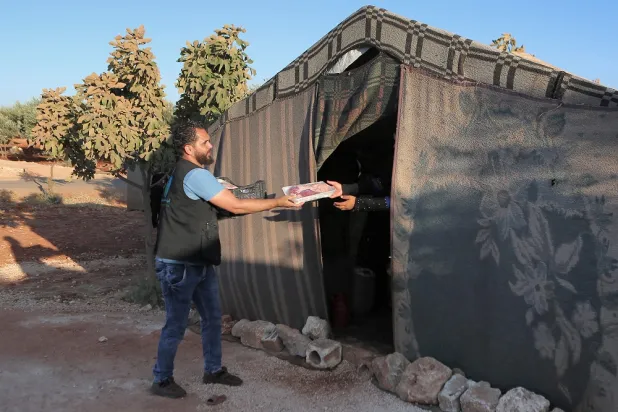A member of the "Emergency Response Team" volunteer group hands out meat freshly-butchered and packaged as part of the commemoration for the Muslim holiday of Eid al-Adha to people at a camp for Syrians displaced by conflict, in the village of Killi in the Syrian opposition-held northwestern city of Idlib on July 10, 2022. (AFP)