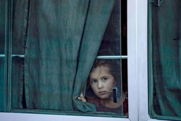 A child from the families linked to ISIS militants looks out the window of a bus after the authorities of the Kurdish units handed them over to Tajikistan in the city of Qamishli on Monday (Asharq Al-Awsat)