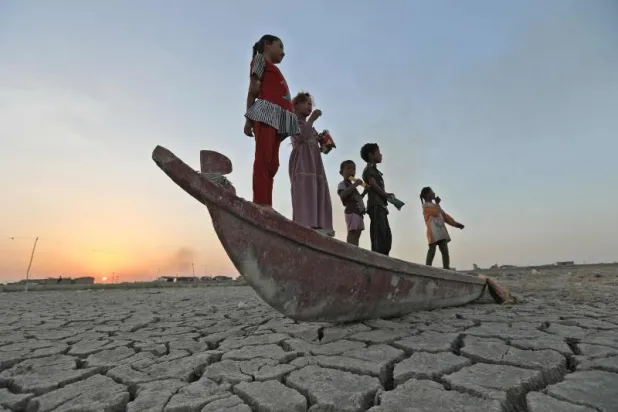 أطفال عراقيون يقفون على مركب راس في مجرى مائي ضربه الجفاف بمحافظة ذي قار (أ.ف.ب)