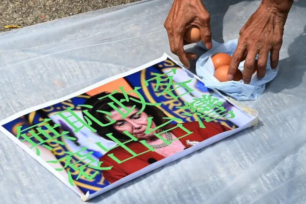 متظاهر يلتقط حبات البيض استعدادا لرشقها على صورة رئيسة مجلس النواب الأميركي نانسي بيلوسي أمام القنصلية الأميركية في هونغ كونغ (أ.ف.ب)