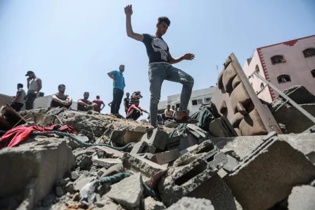 فلسطينيون على أنقاض مبنى دمرته غارة جوية إسرائيلية (د.ب.أ)