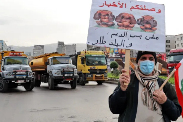 A Lebanese protester holds a sign as fuel tankers block a road in Beirut during a general strike by public transport and workers' unions over the country's economic crisis [File: Anwar Amro/AFP]