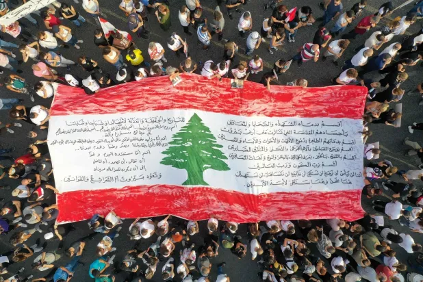 This aerial view shows activists and relatives of the 2020 Beirut port blast victims spreading a giant national flag, as they march in the Lebanese capital's port area on August 4, 2022, on the day that crisis-hit country marks two years since a giant explosion ripped through the capital. (AFP)