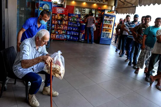 An elderly man rests outside after buying a bag of subsidized flatbread, as others continue to wait in a queue, in the Lebanese capital Beirut on July 29, 2022, amid a shortage of wheat supplies. (AFP)